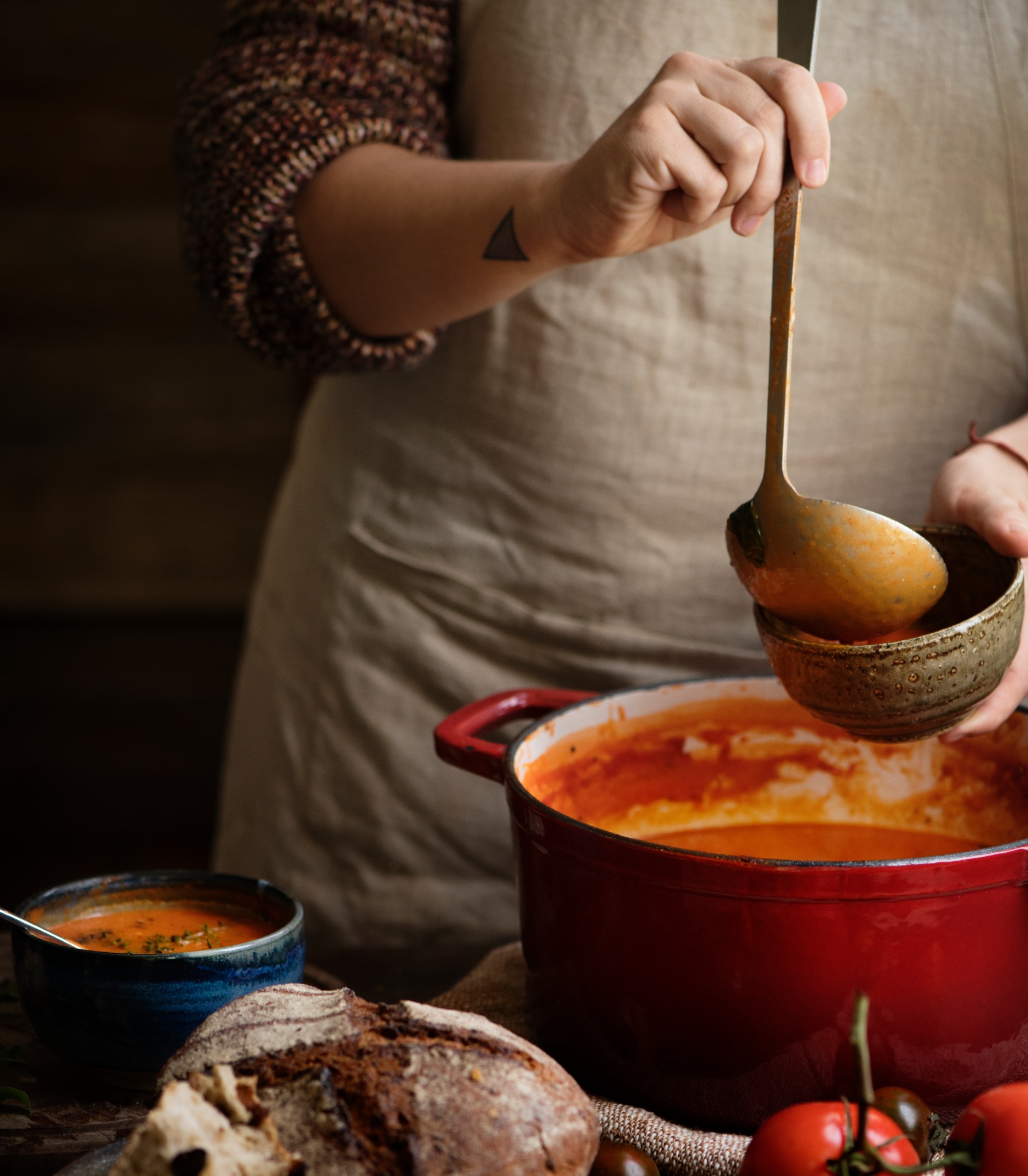 Soup being ladled from a red pot into a ceramic bowl, with rustic bread nearby